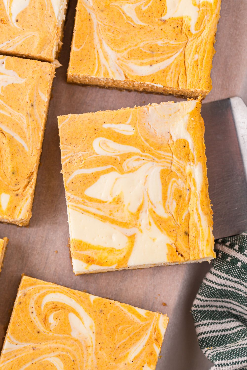 sliced Swirled Pumpkin Cheesecake Bars on table with a spatula under one