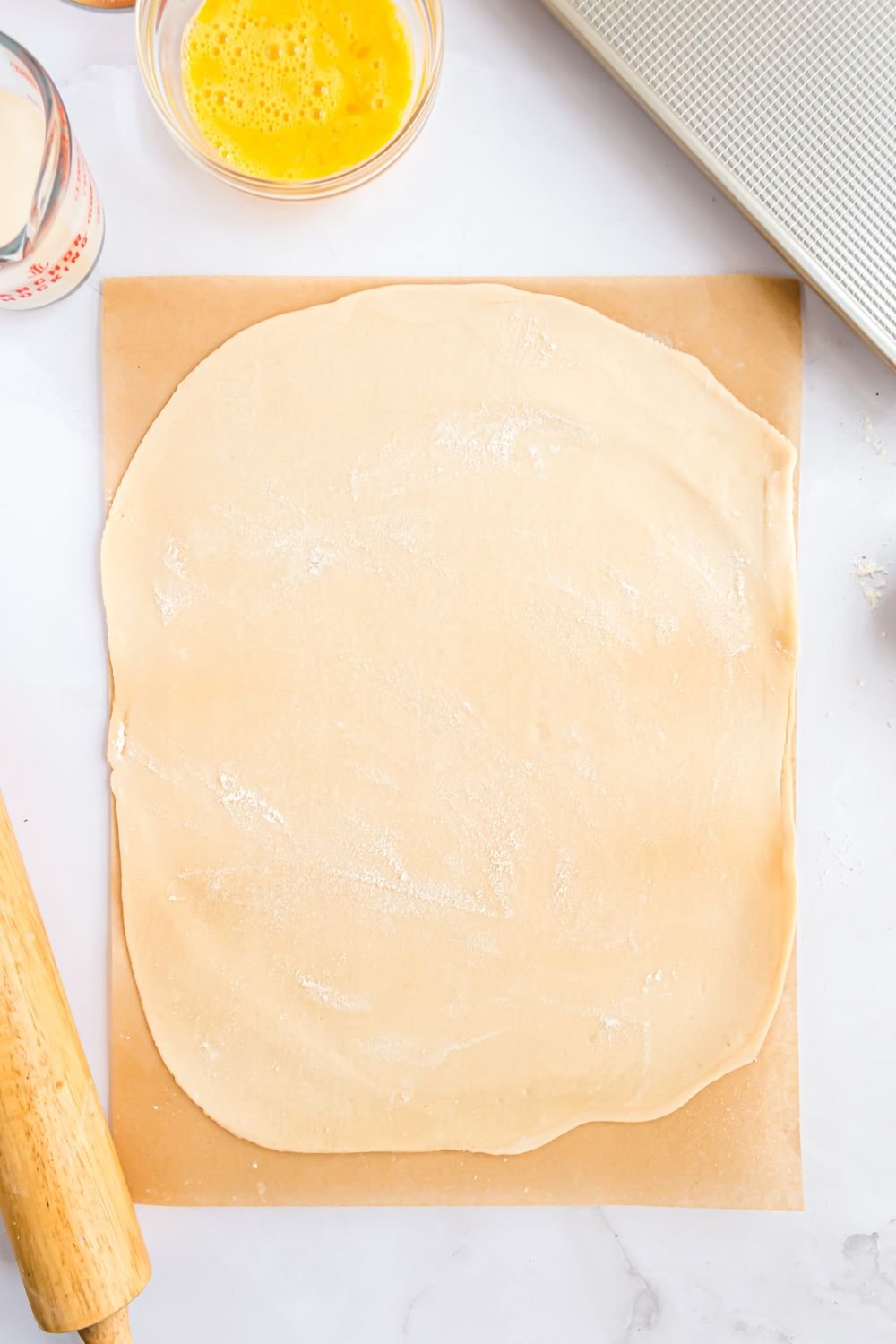 pie crust sitting on a wooden cutting board being rolled out into a thin rectangle shape for making Sheet Pan Pumpkin Pie