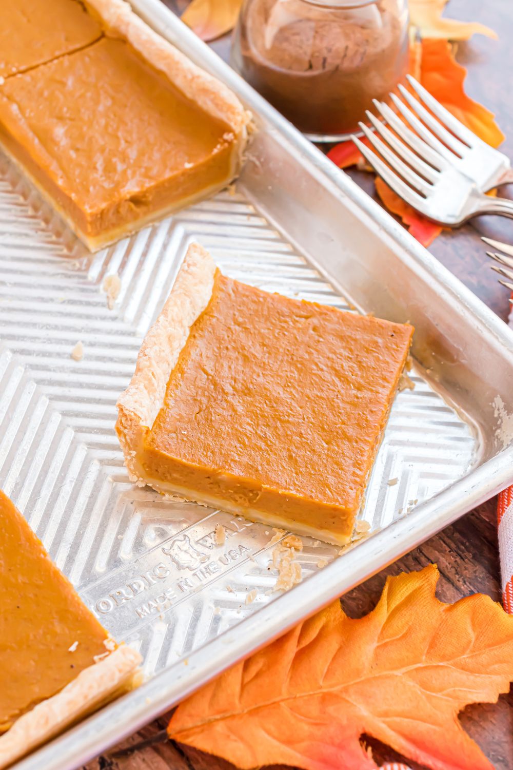 metal pan on a wooden table decorated with rustic theme, with slices of Sheet Pan Pumpkin Pie inside the pan cut into squares 