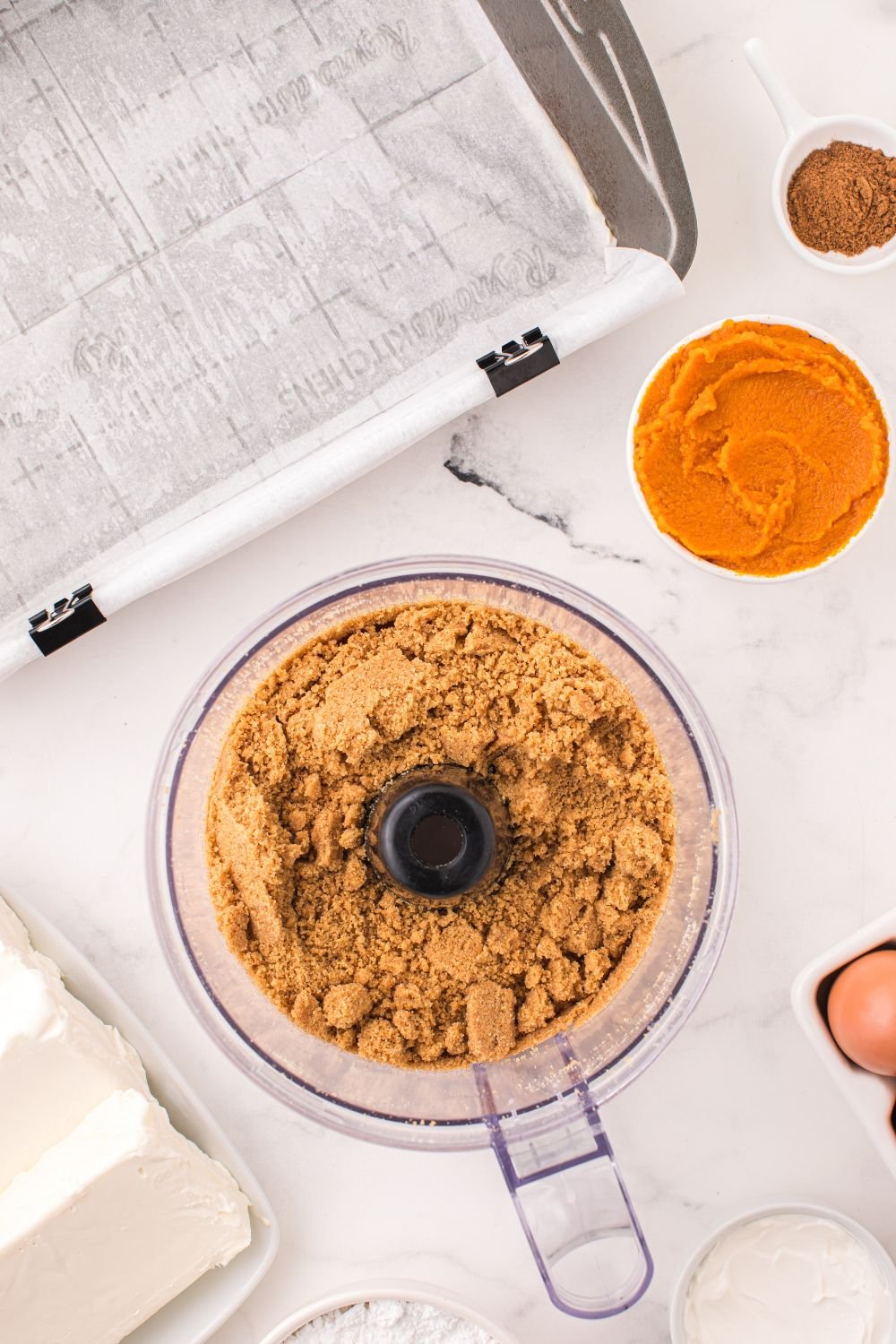 graham crackers in a food processor crushed, and pumpkin puree in bowl next to it