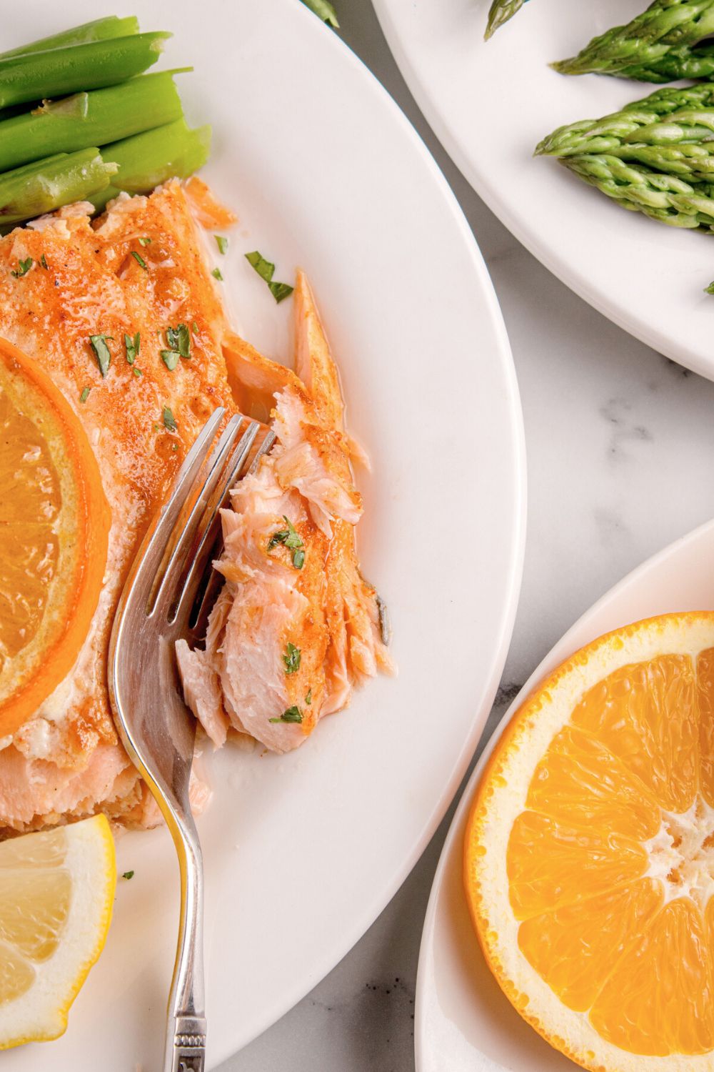 Grilled Honey Mustard Salmon on plate with a fork biting into a piece of it with asparagus on a second plate 
