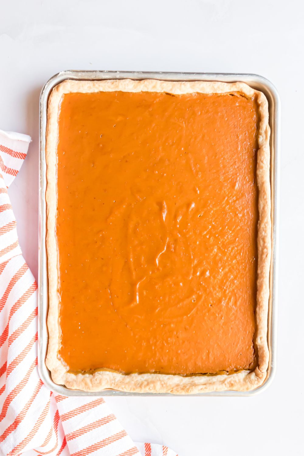 baked Sheet Pan Pumpkin Pie sitting on a white table with a red and white striped towel to the side