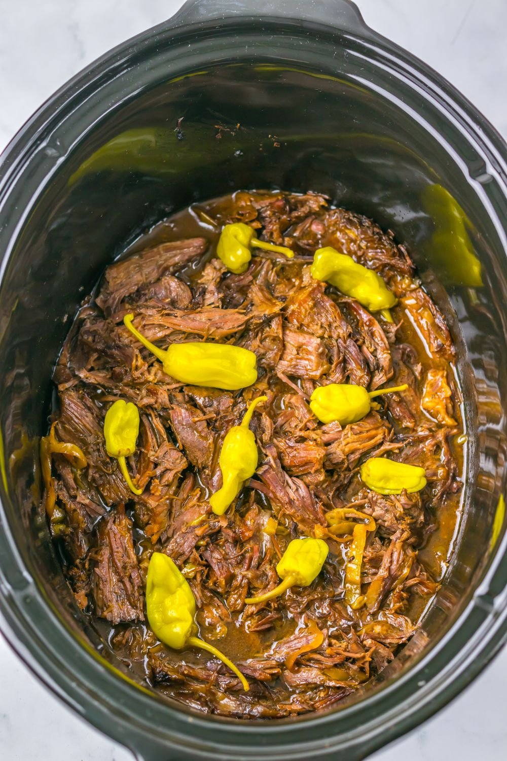 Slow Cooker Mississippi Pot Roast in a slow cooker with more peppers on top 
