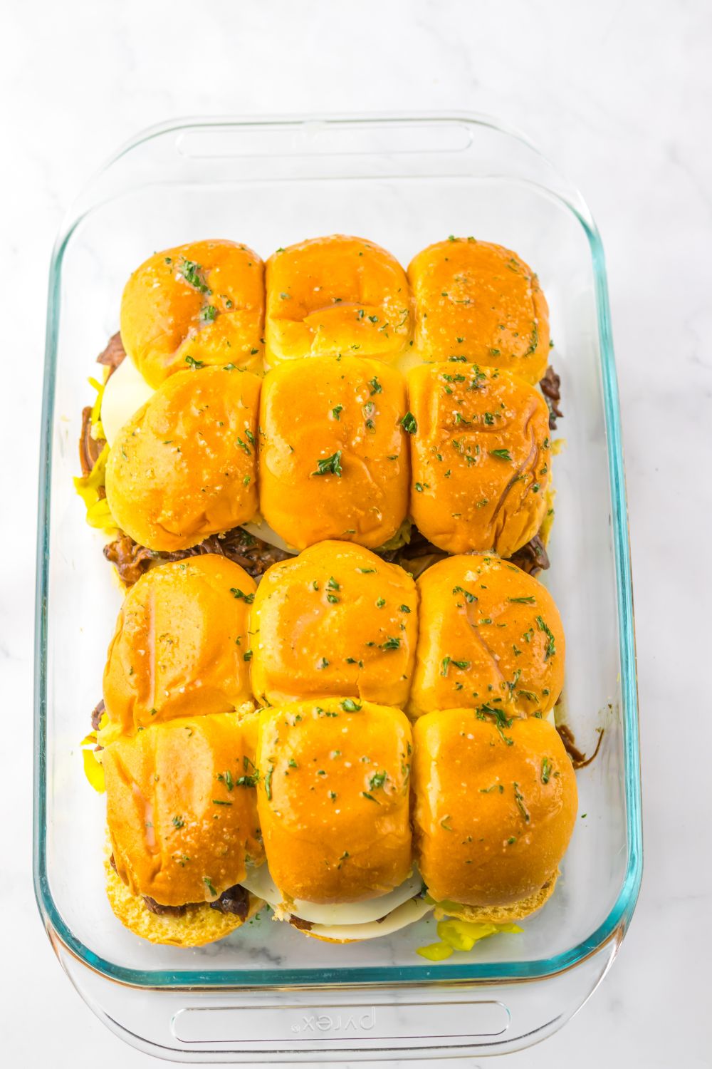 Slow Cooker Mississippi Pot Roast Sliders assembled and being topped with parsley butter