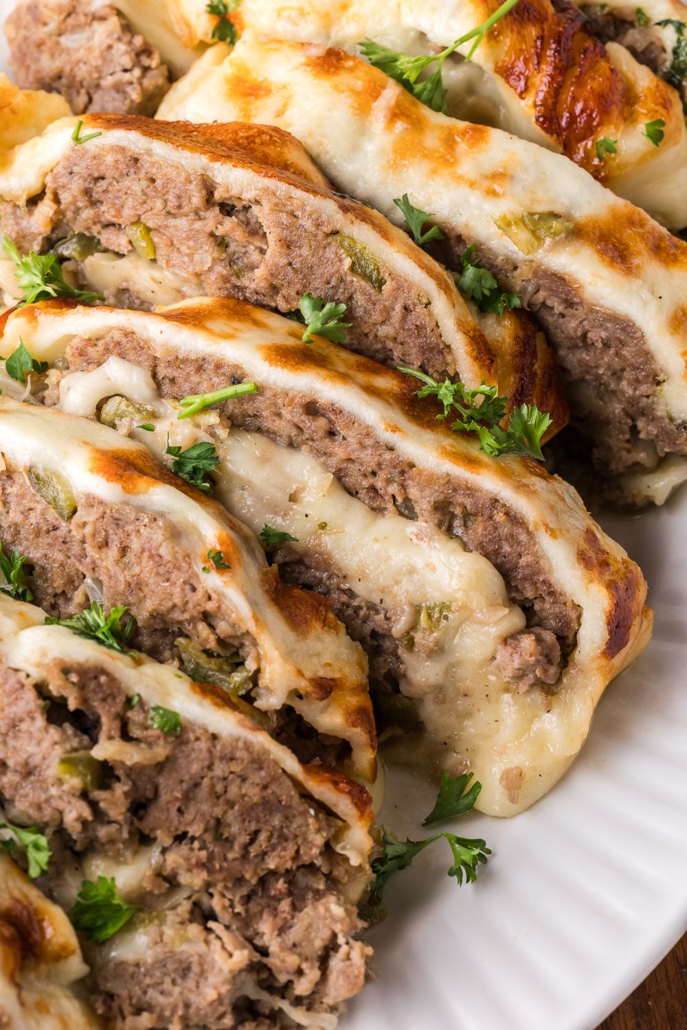 sliced Stuffed Philly Cheesesteak Meatloaf on a white platter that is sprinkled with parsley on top of meatloaf