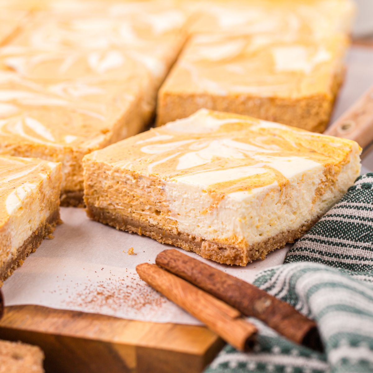 Swirled Pumpkin Cheesecake Bars placed on table with cinnamon sticks in front of bars