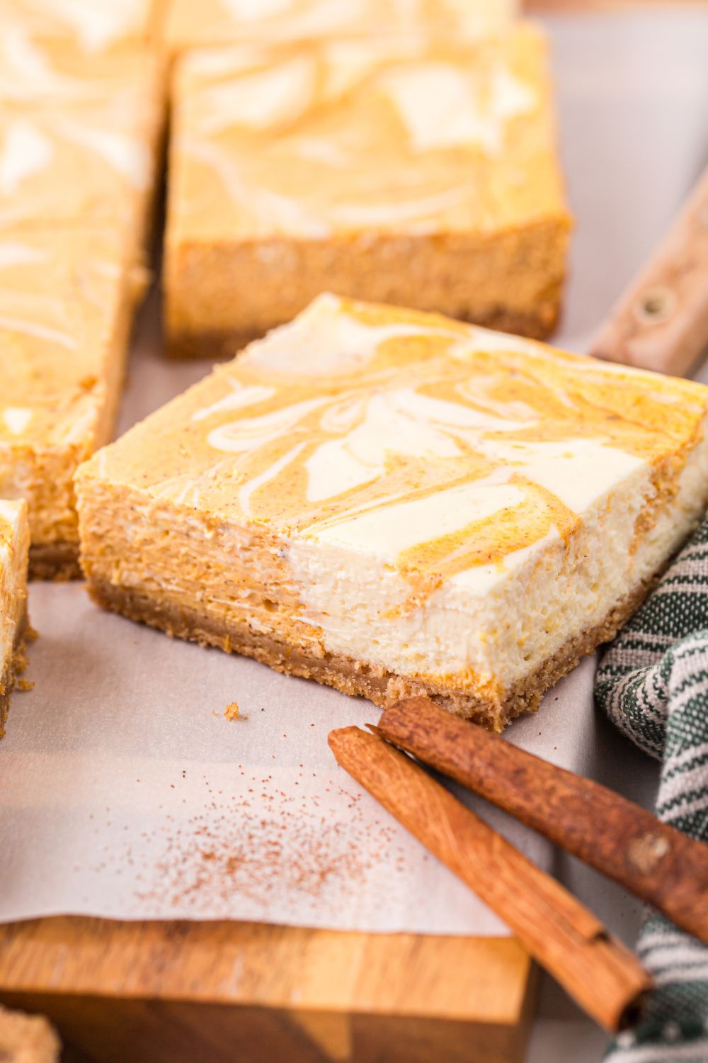Swirled Pumpkin Cheesecake Bars placed on a table with some cinnamon sticks in front