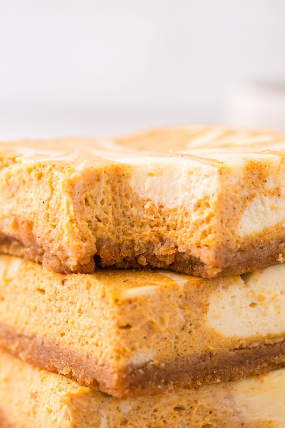 view of Swirled Pumpkin Cheesecake Bars stacked on top of one another with a bite taken out of top bar