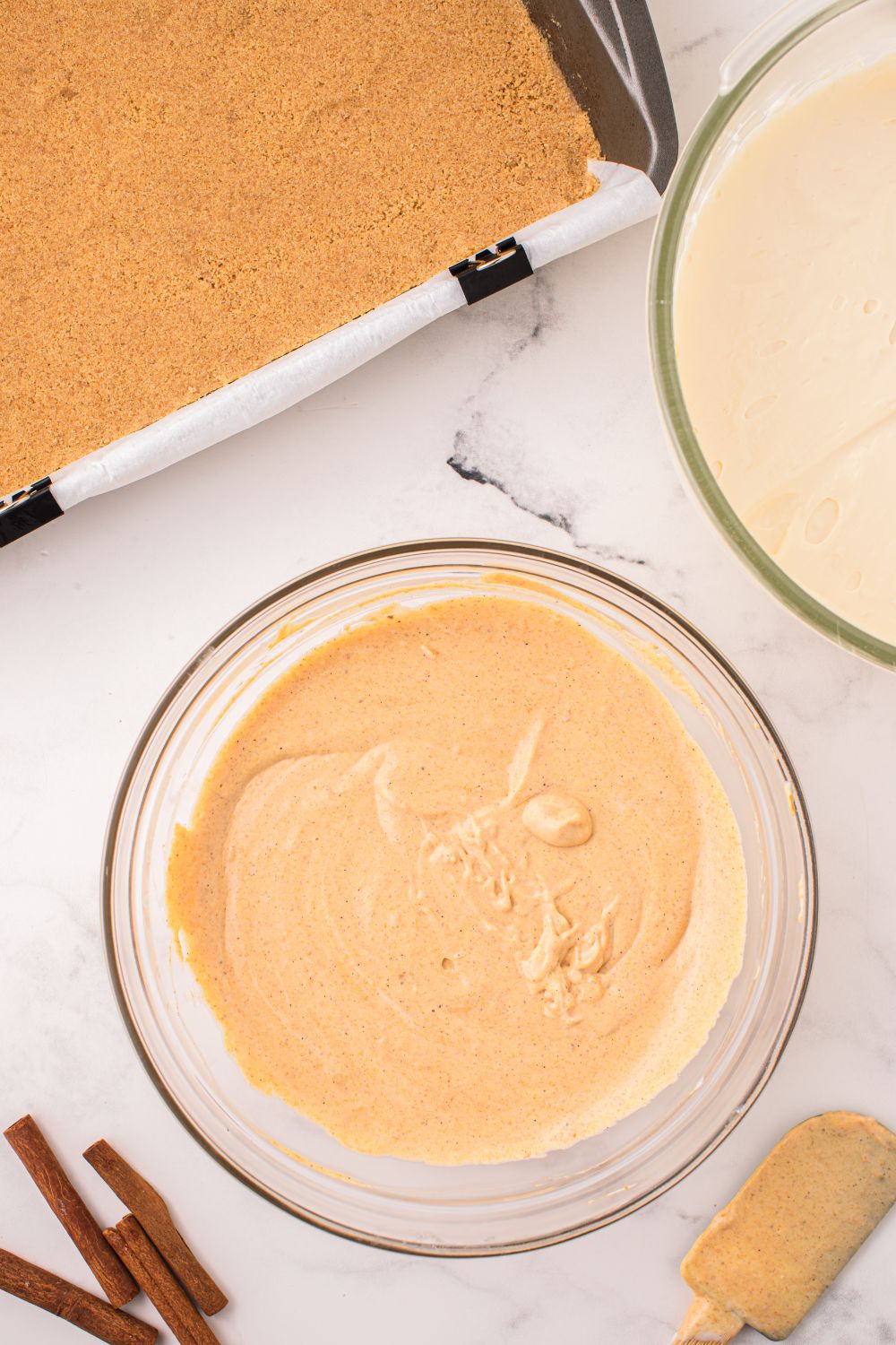 bowl of cheesecake batters and pan of graham cracker crumbs