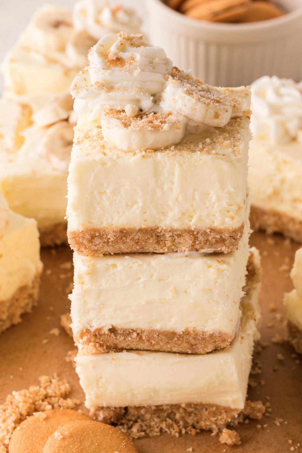 No Bake Banana Pudding Cheesecake Bars stacked on a plate with more bars all around the table 