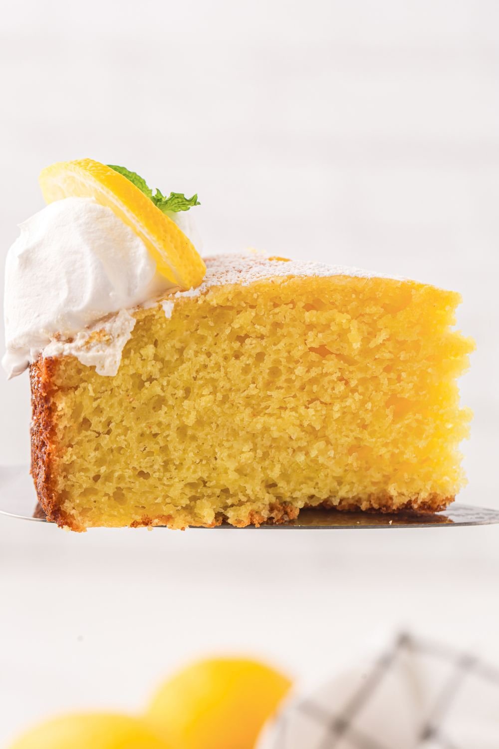 Italian Lemon Ricotta Cake sliced and view of it on plate from the side topped with whipped cream