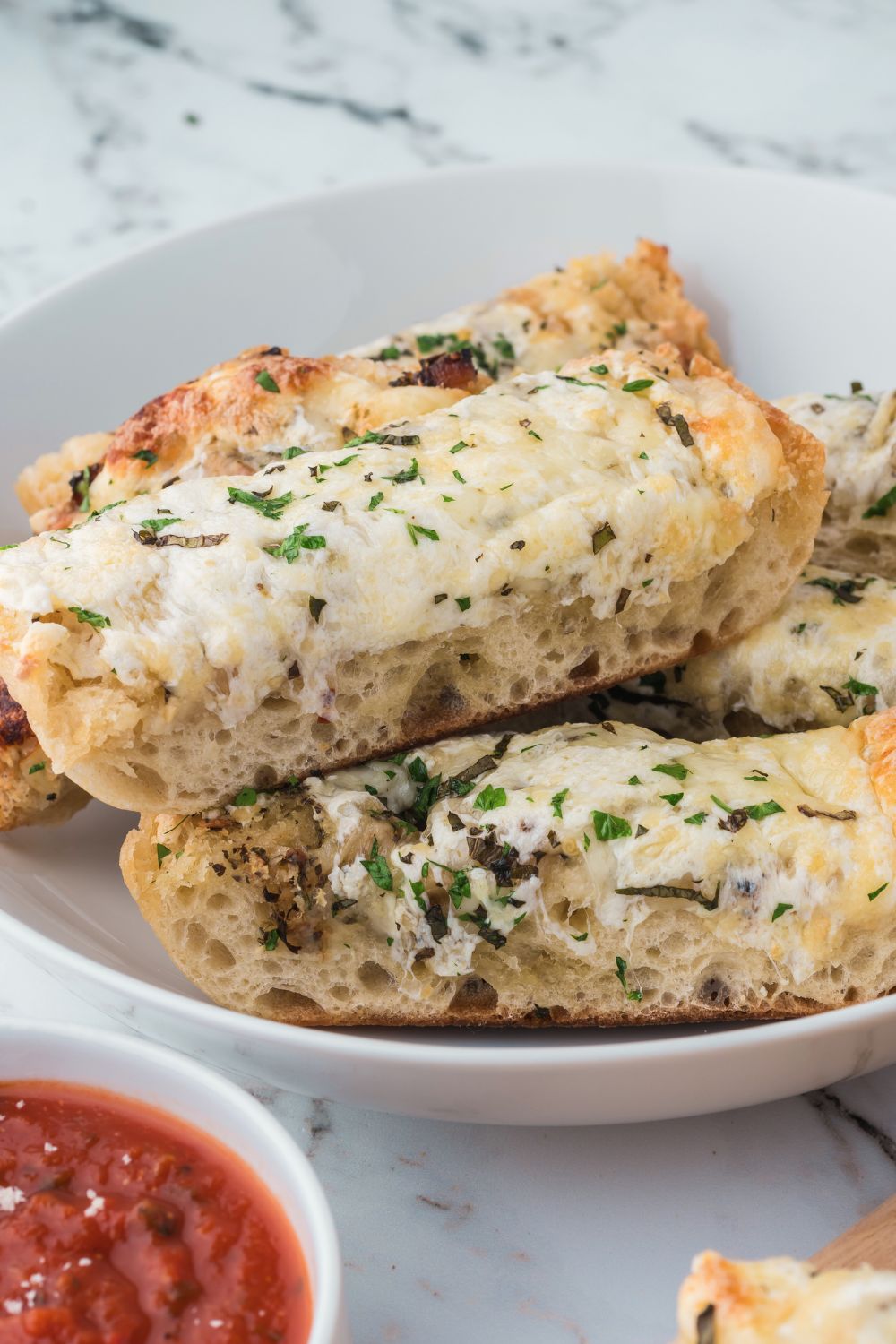 stack of Cheesy Garlic Bread on plate with a bowl of marinara sauce in front of plate 