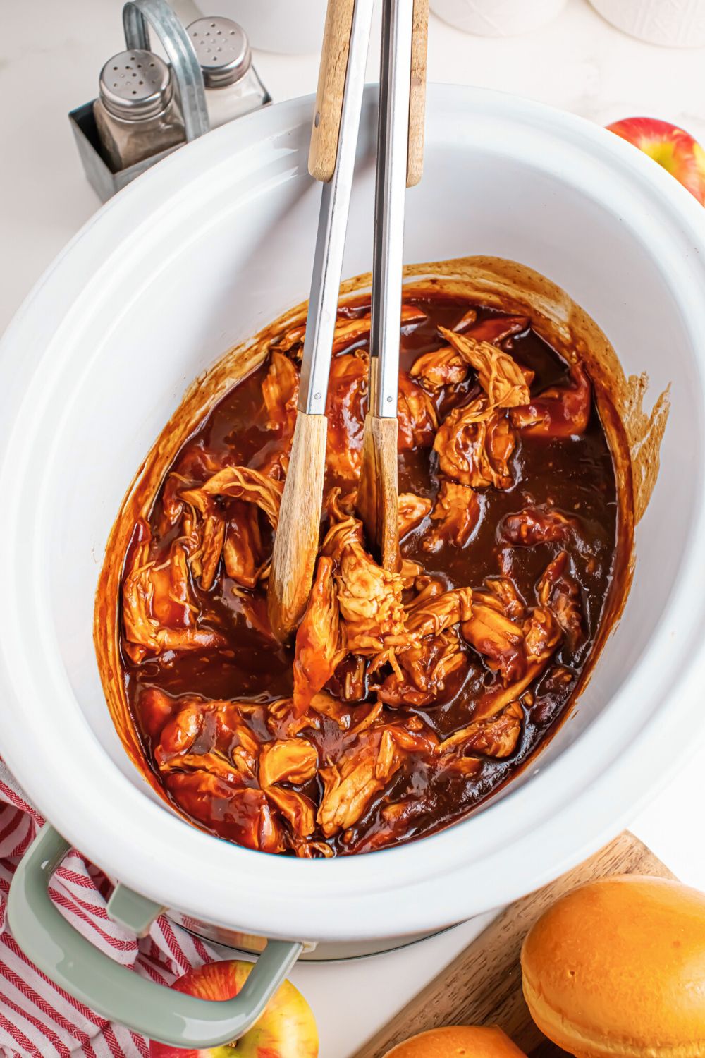 Crockpot Apple Butter BBQ Pulled Chicken in a crockpot sitting on table with tongs sitting inside the slow cooker