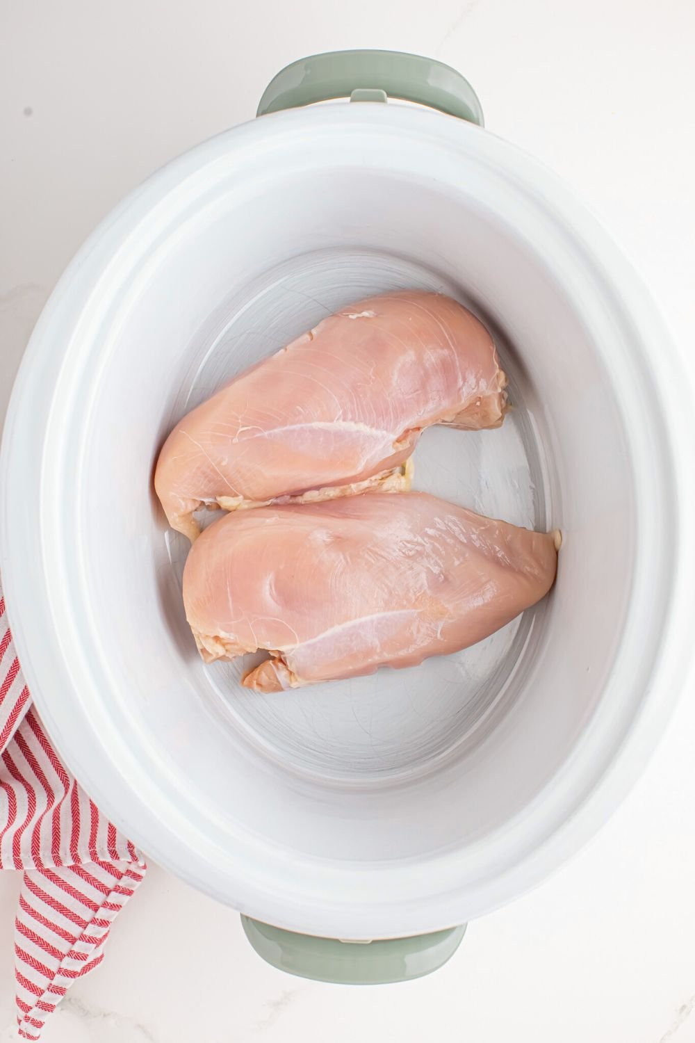 2 raw chicken breast in crockpot sitting on table