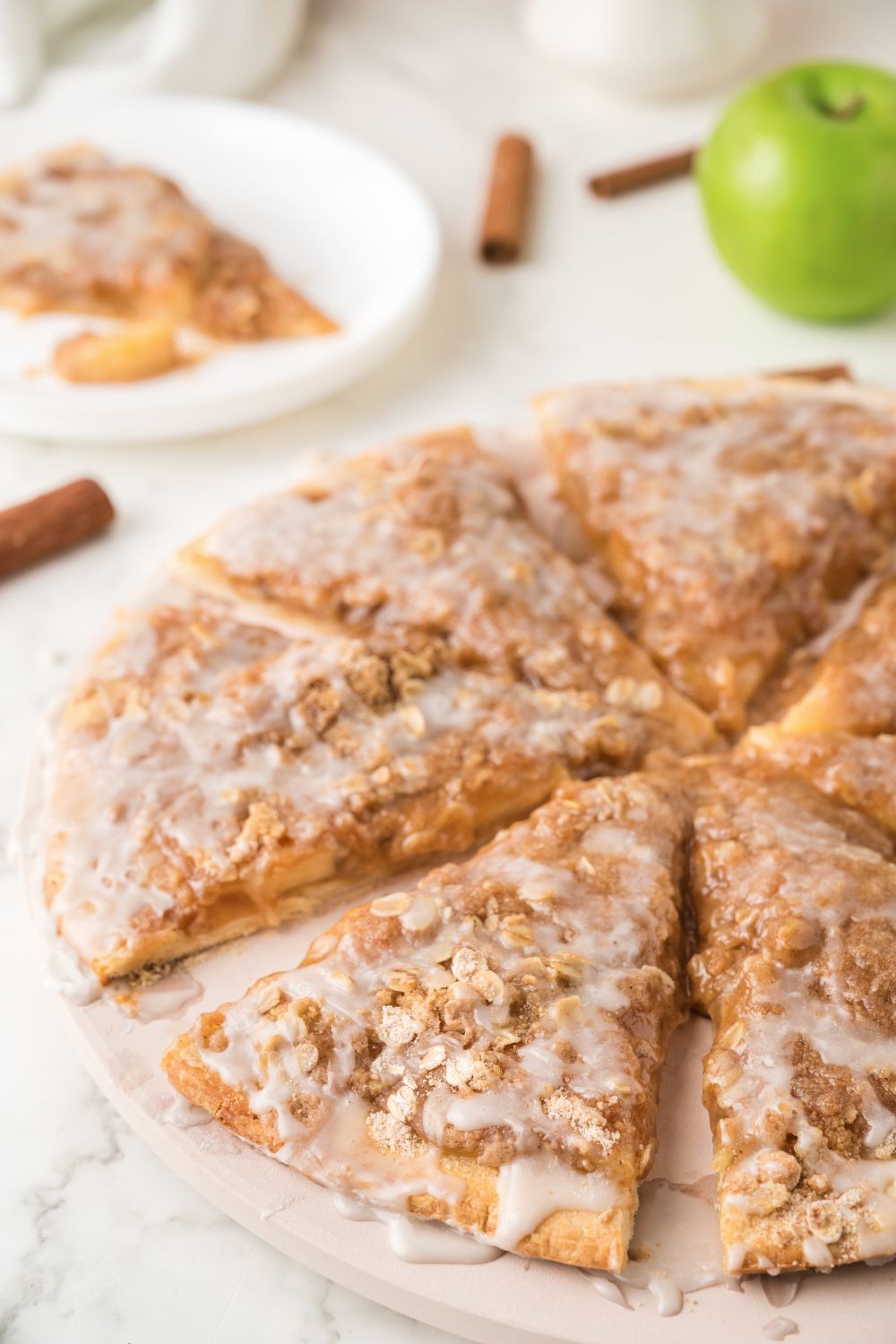 Apple Pie Pizza sliced and placed on table with apples and cinnamon sticks behind it on table 