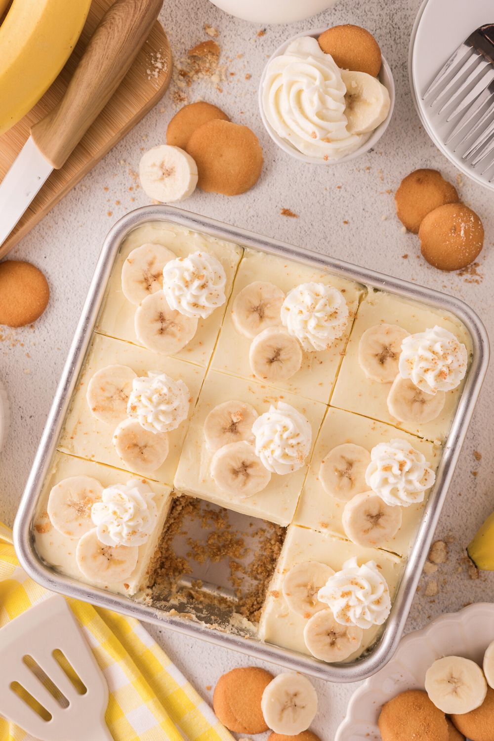 overhead look of table with No Bake Banana Pudding Cheesecake Bars in a pan with one taken out of the pan 