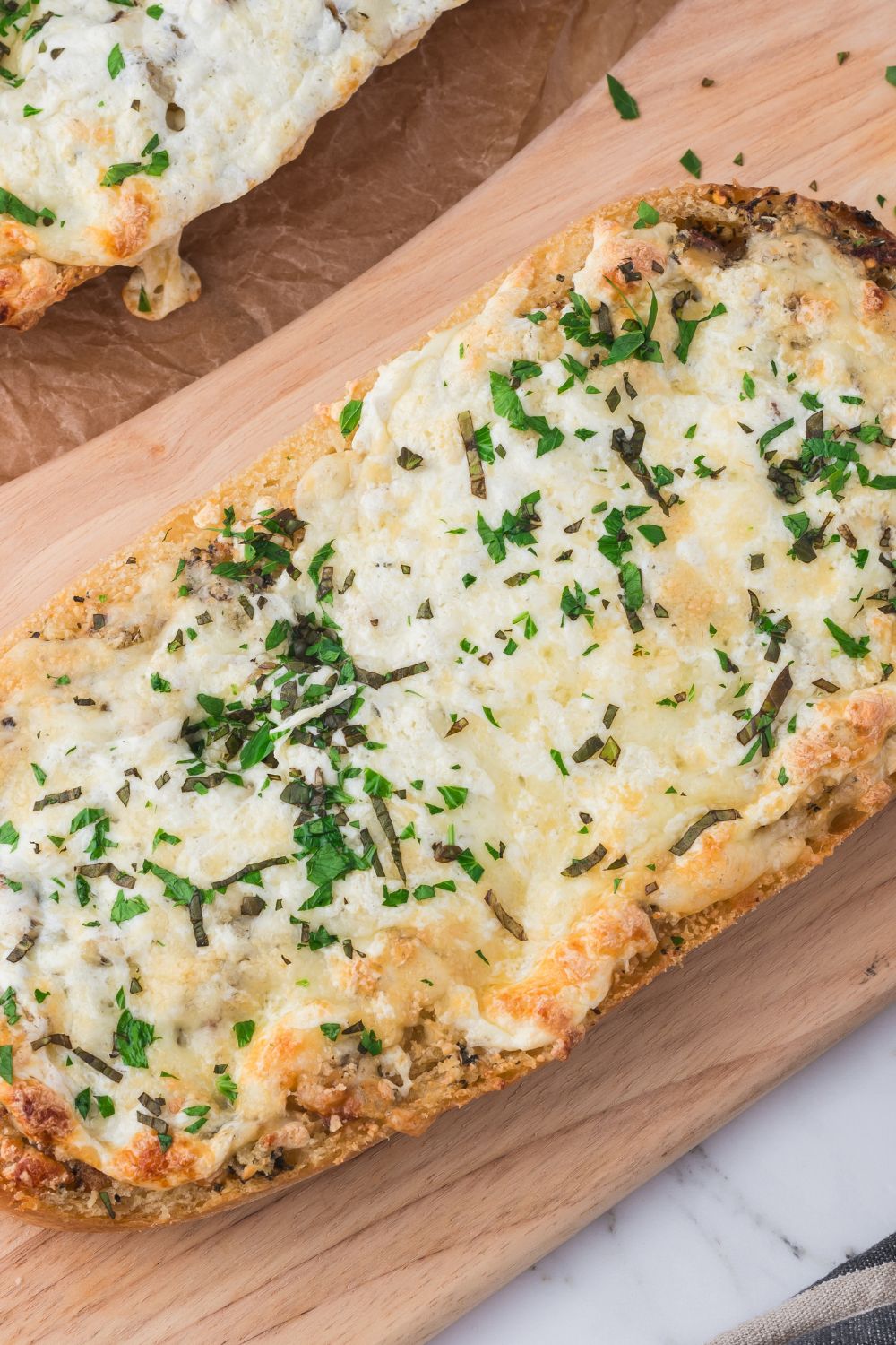 overhead look of table with a piece of Cheesy Garlic Bread on a cutting board topped with parsley 