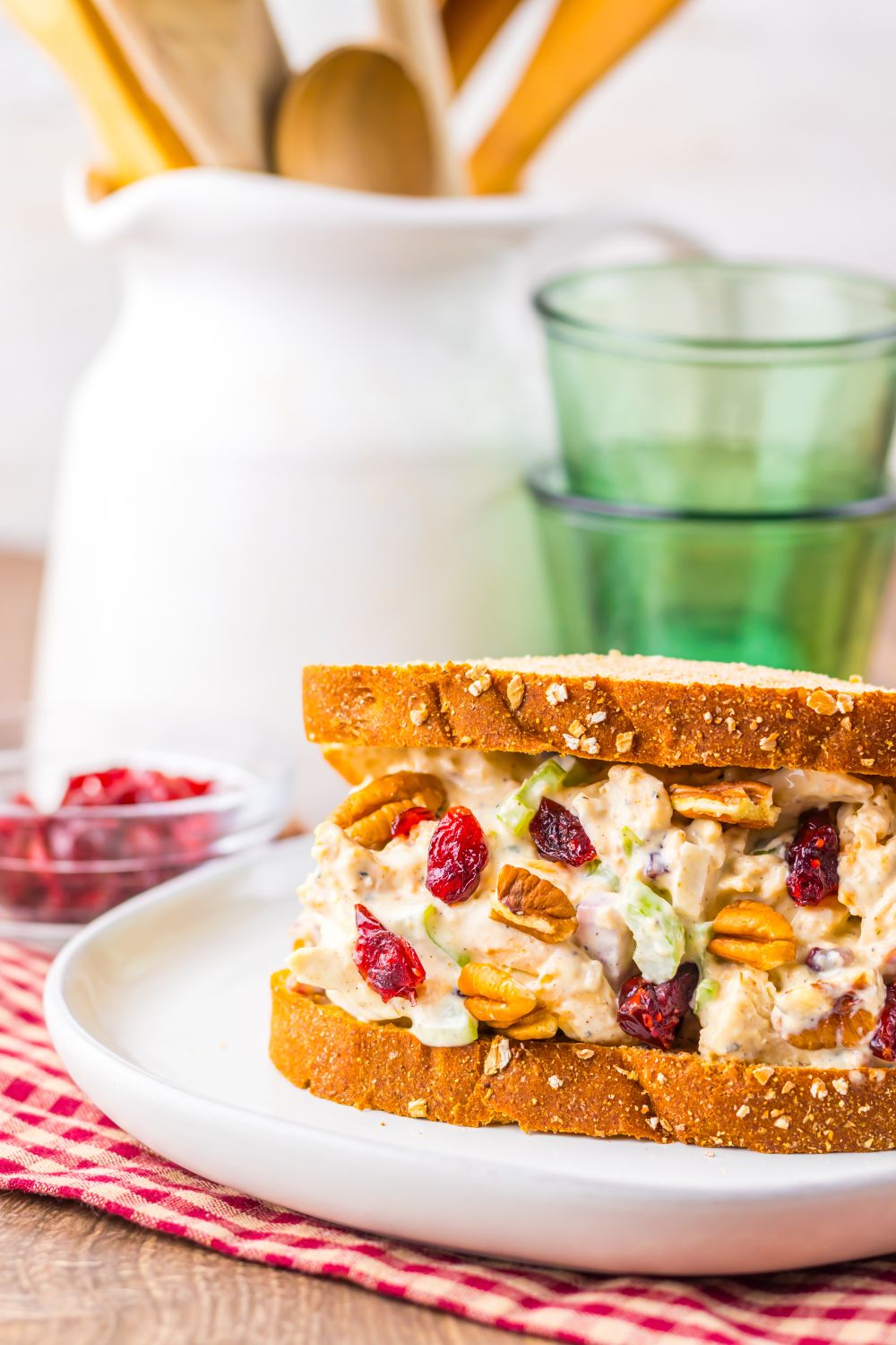 Turkey salad sandwich with cranberries, pecans, and celery on whole grain bread, served on a white plate with a rustic kitchen background