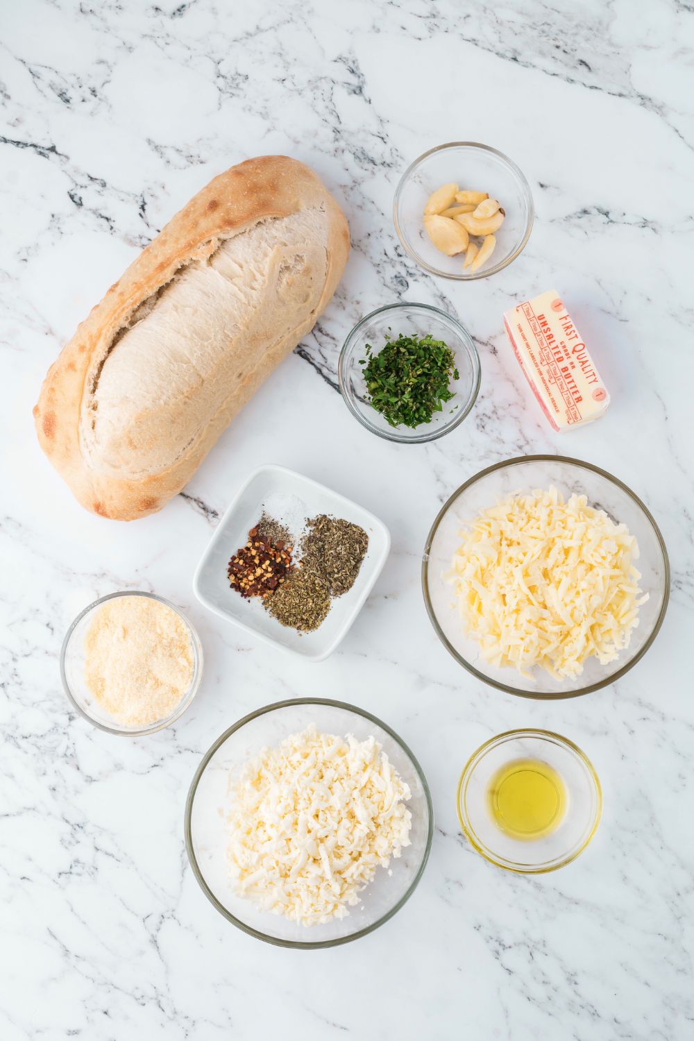 ingredients for Cheesy Garlic Bread on table in single serve containers on marble table 