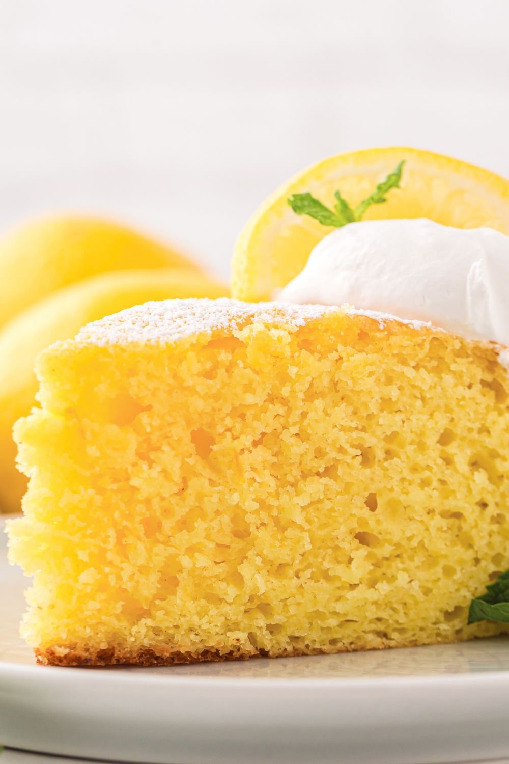 Italian Lemon Ricotta Cake sliced on plate with a dollop of whipped cream on top and a fresh lemon slice 