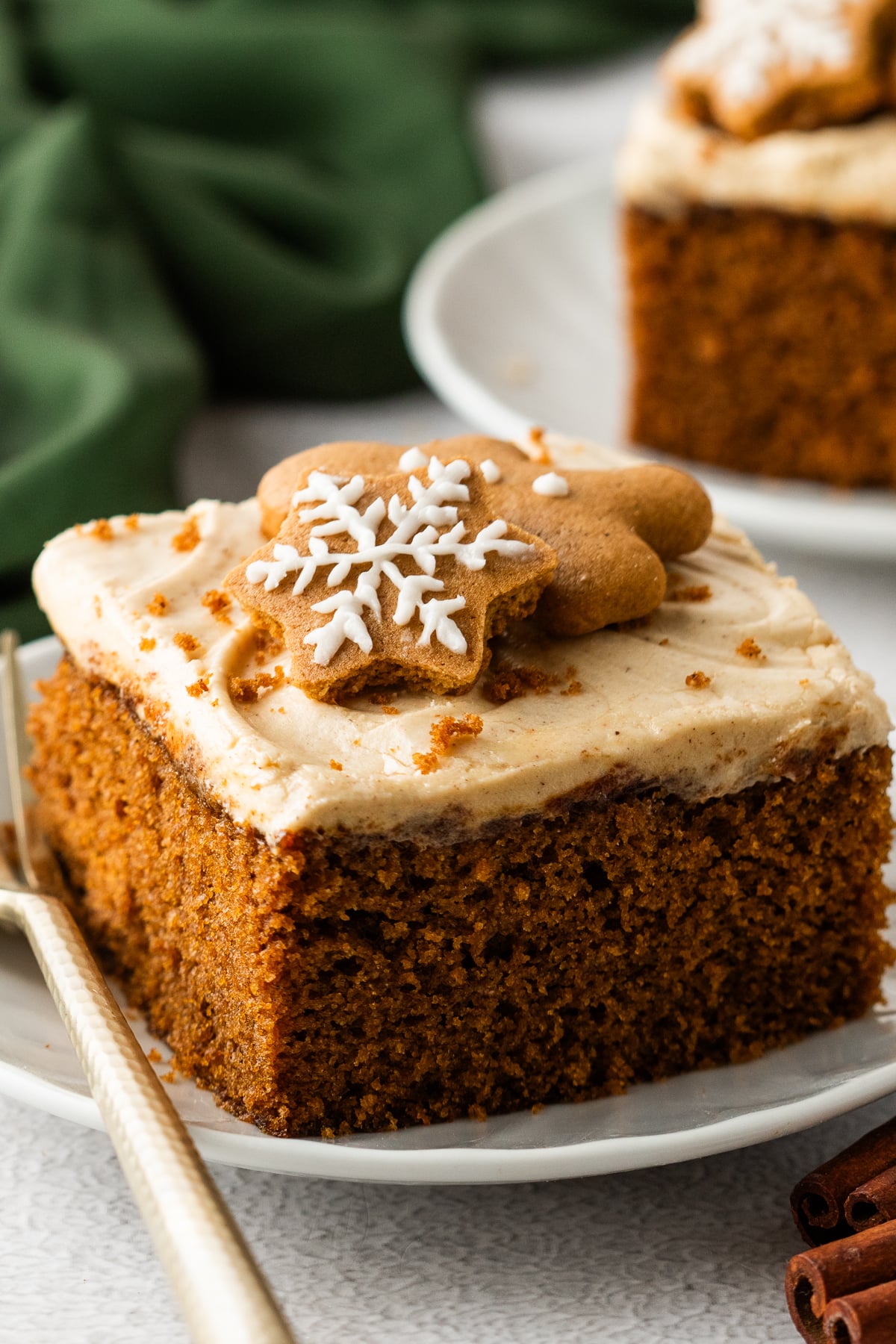 Up close shot of the Gingerbread Cake with Cream Cheese Frosting on white plates with a gold fork next to the slice 