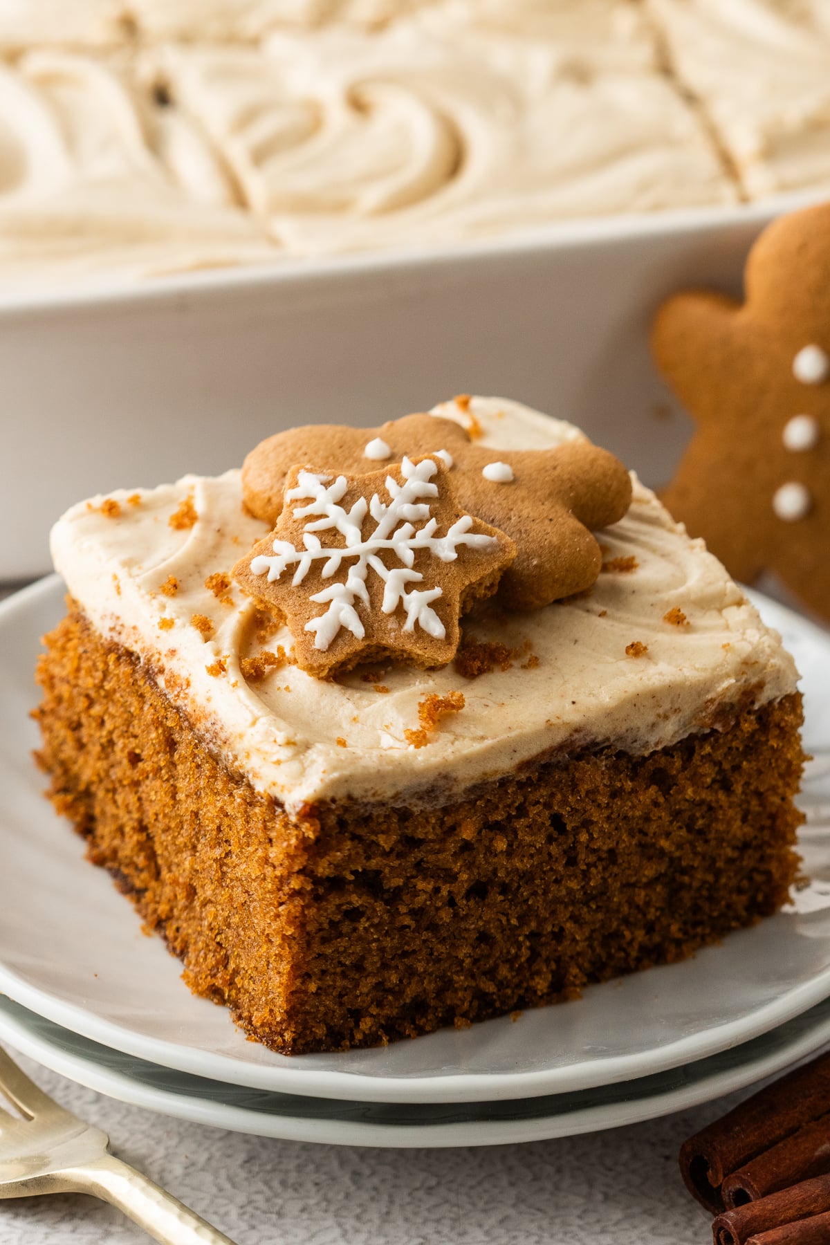 slice of Gingerbread Cake with Cream Cheese Frosting on a white plate with the whole cake pan behind 