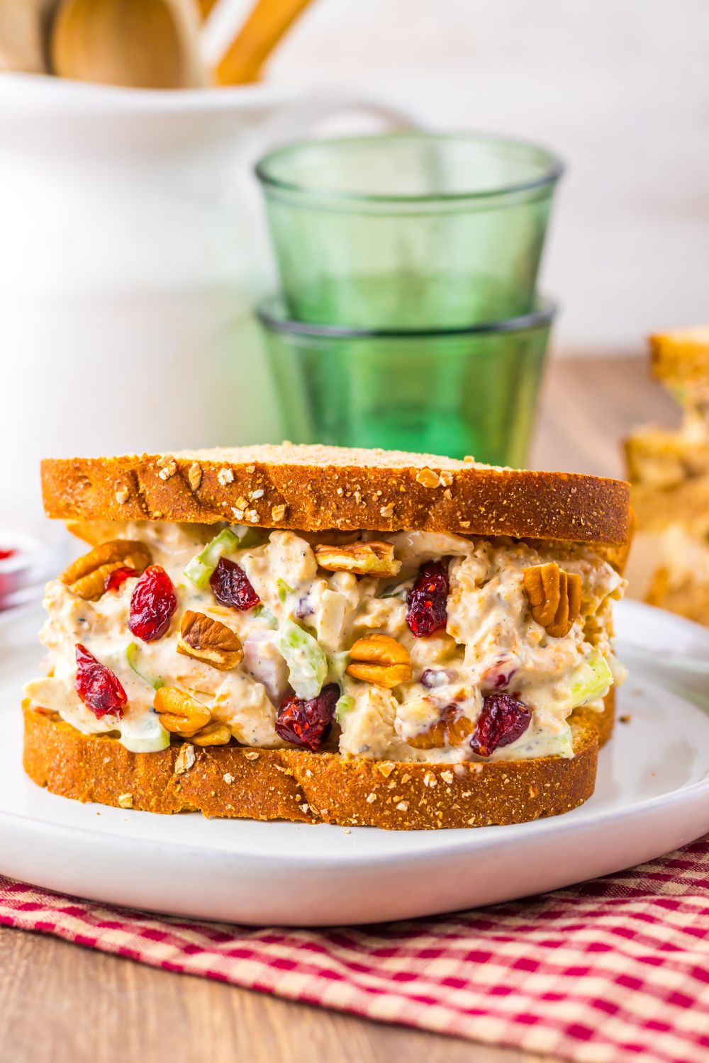 front view of wooden table with a plate with a thick Thanksgiving Turkey Salad sandwich on plate, and two glasses stacked together sitting behind it on the table 