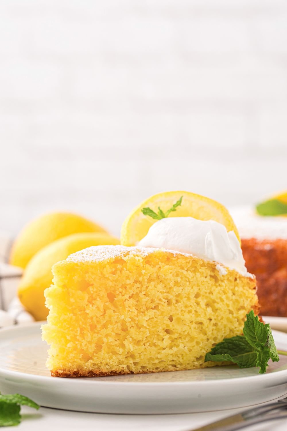 side view of table with a slice of Italian Lemon Ricotta Cake on plate with mint leaf to side of plate 