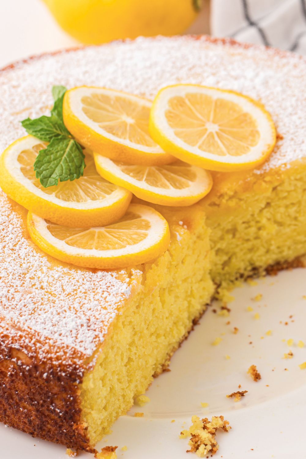 Italian Lemon Ricotta Cake on table with a few slices taken out of it and lemon wedges on top 