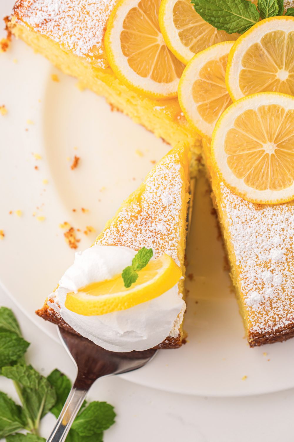 Italian Lemon Ricotta Cake being lifted off the cake platter with more sitting on table 