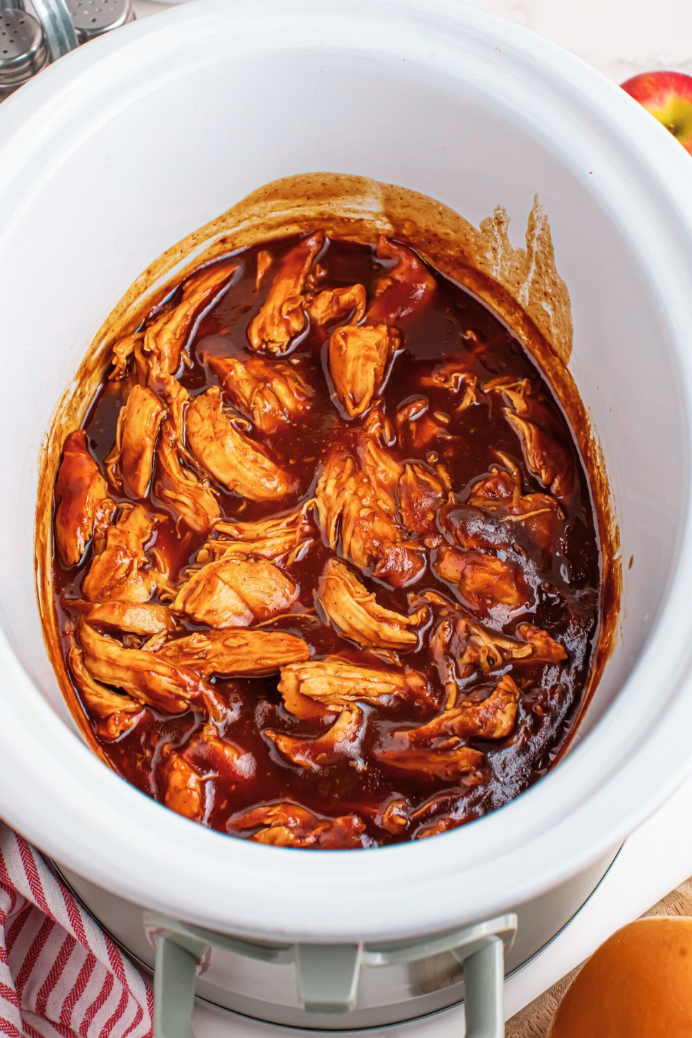 Crockpot with Apple Butter BBQ Pulled Chicken inside sitting on table with a towel to the side 