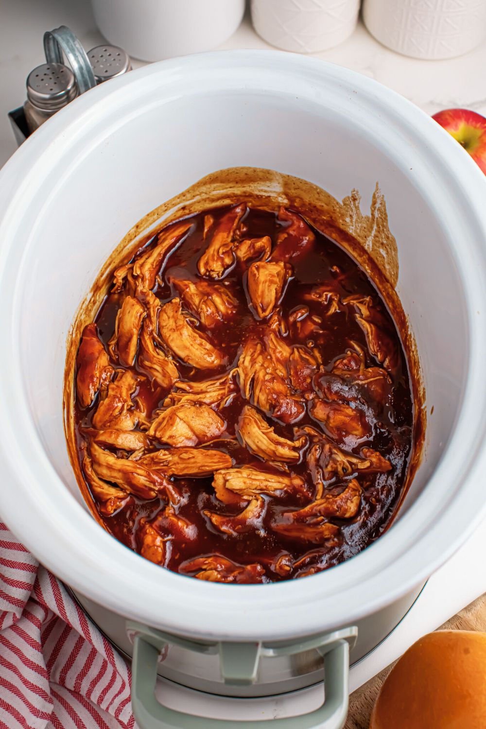 overhead look of crockpot on table with salt and pepper shakers behind it with Crockpot Apple Butter BBQ Pulled Chicken inside 