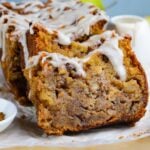 Amish Apple Fritter Bread sliced and placed on a parchment paper on table with a bowl with glaze to the side
