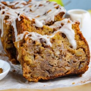 Amish Apple Fritter Bread sliced and placed on a parchment paper on table with a bowl with glaze to the side