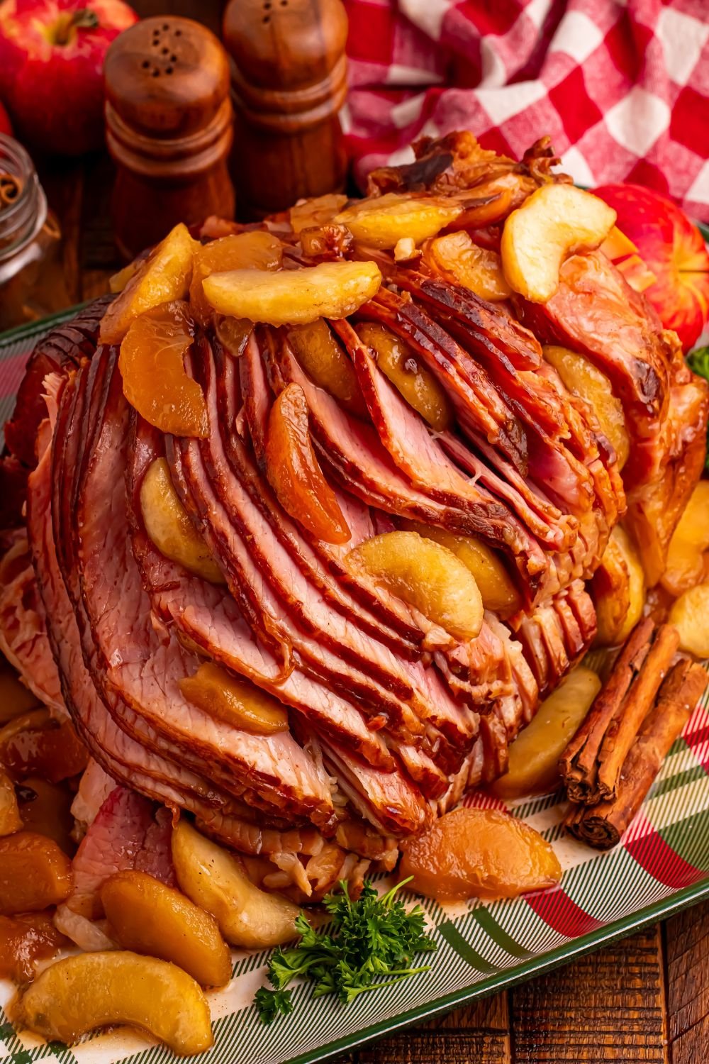 Slow Cooker Apple Glazed Ham on a plaid platter sitting on table with a checkered red towel behind ham, salt and pepper shakers 