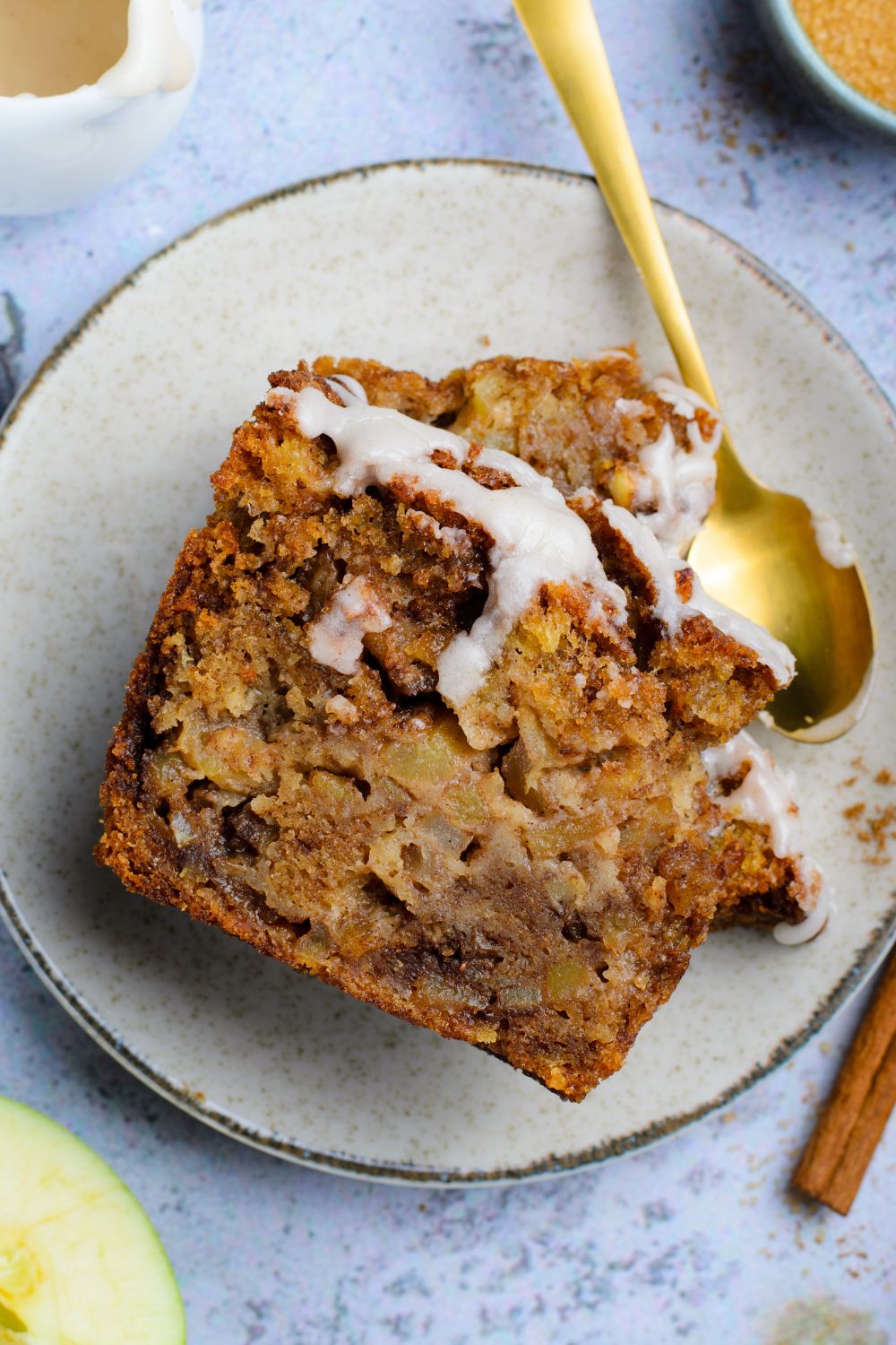two slices of Amish Apple Fritter Bread on plate with a spoon to side of plate with a few bites taken out sitting on blue table 