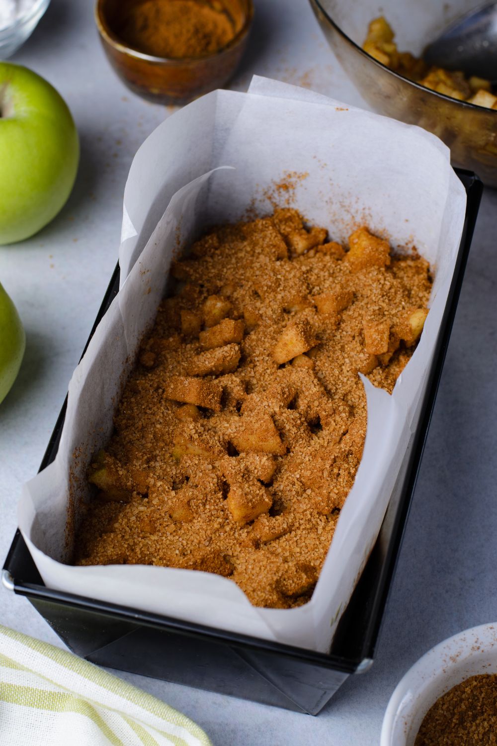 cinnamon mixture and diced apples inside a loaf pan sitting on marble table with green apples to side of pan 