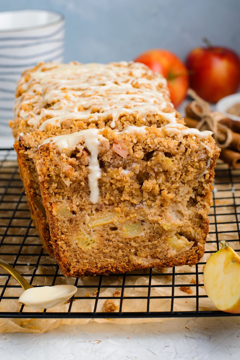 metal cooling rack with parchment paper under it sitting on table with a loaf of Apple Cinnamon Loaf Cake sliced and topped with a white glaze 