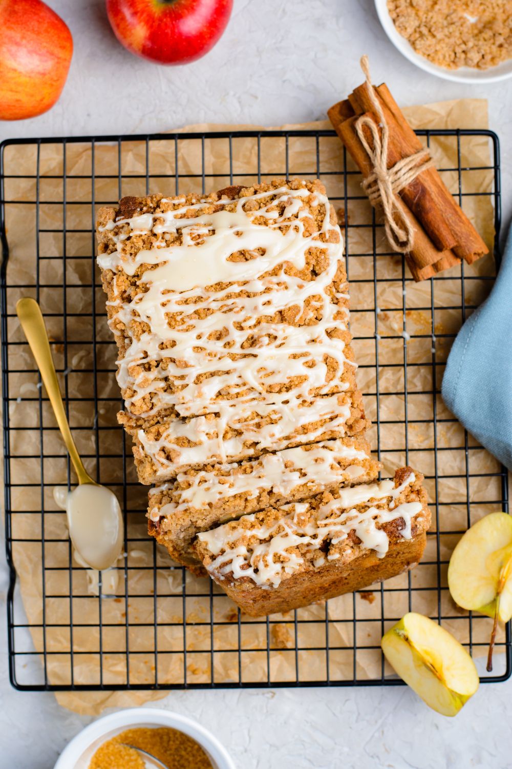 Apple Cinnamon Loaf Cake on a cooling rack on marble counter with a bundle of cinnamon sticks to the side, apples, sliced apples and more to decorate it for fall 