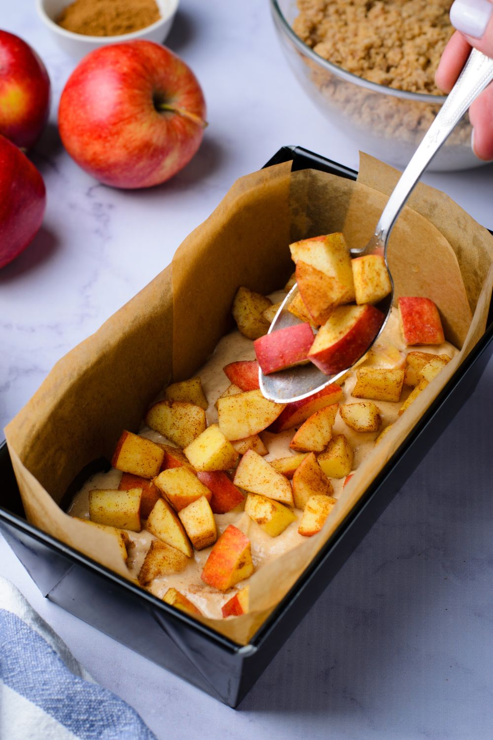cinnamon cubed apples being put into the loaf pan on top of batter for making Apple Cinnamon Loaf Cake