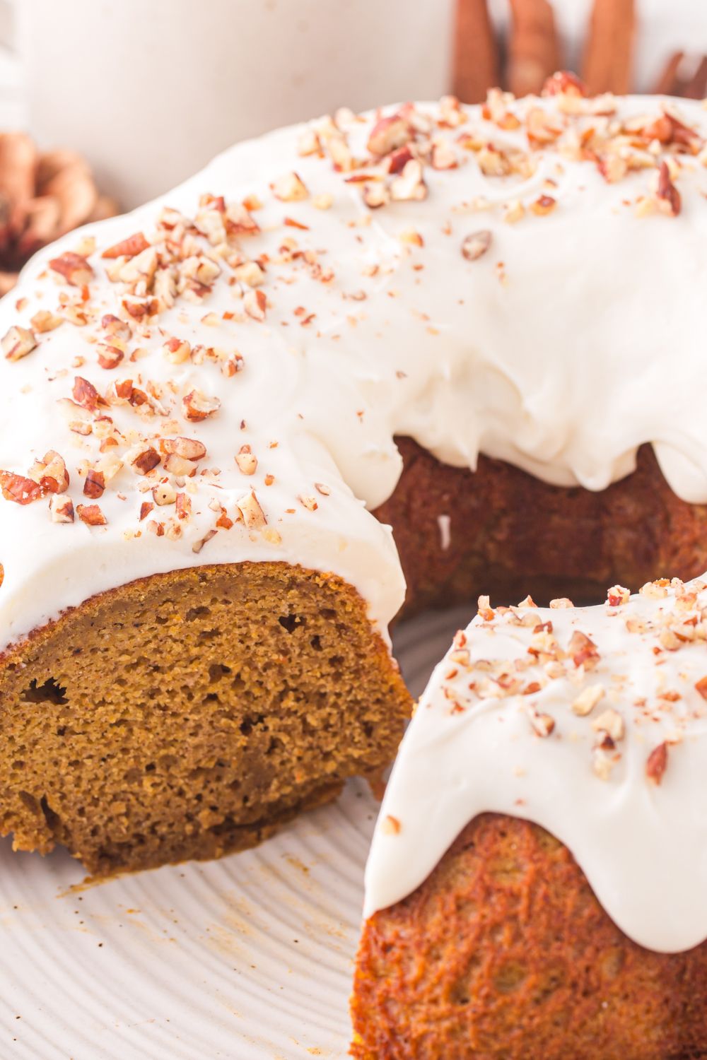 Pumpkin Bundt Cake on a white platter with nuts on top. A few pieces are sliced out of the cake 