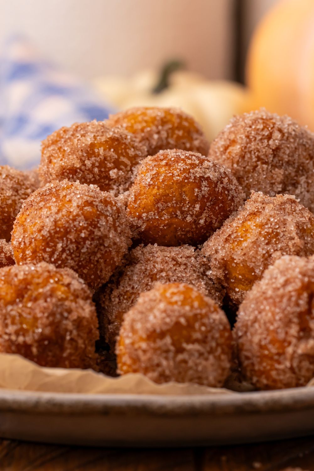 side view of Pumpkin pie donut holes  in a bowl on table with a blue checkered towel in the background of picture 