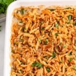 Green Bean Casserole in a white casserole dish sitting on table with fresh parsley sprinkled on top of casserole