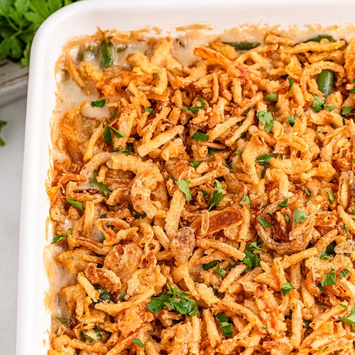 Green Bean Casserole in a white casserole  dish sitting on table with fresh parsley sprinkled on top of casserole 