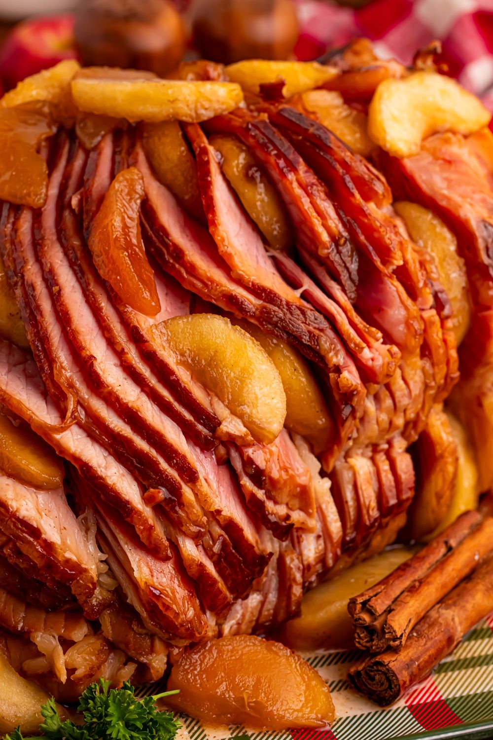 side view of a Slow Cooker Apple Glazed Ham sitting on a platter with cinnamon sticks in front 