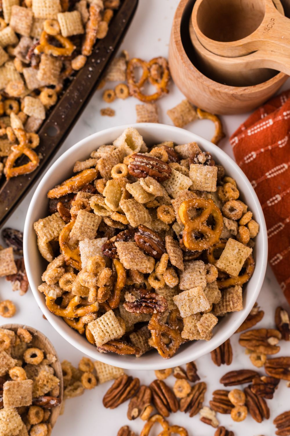 Pumpkin Spice Chex Mix scattered around a table with a bowl full of snack mix, and a sheet pan off to the side