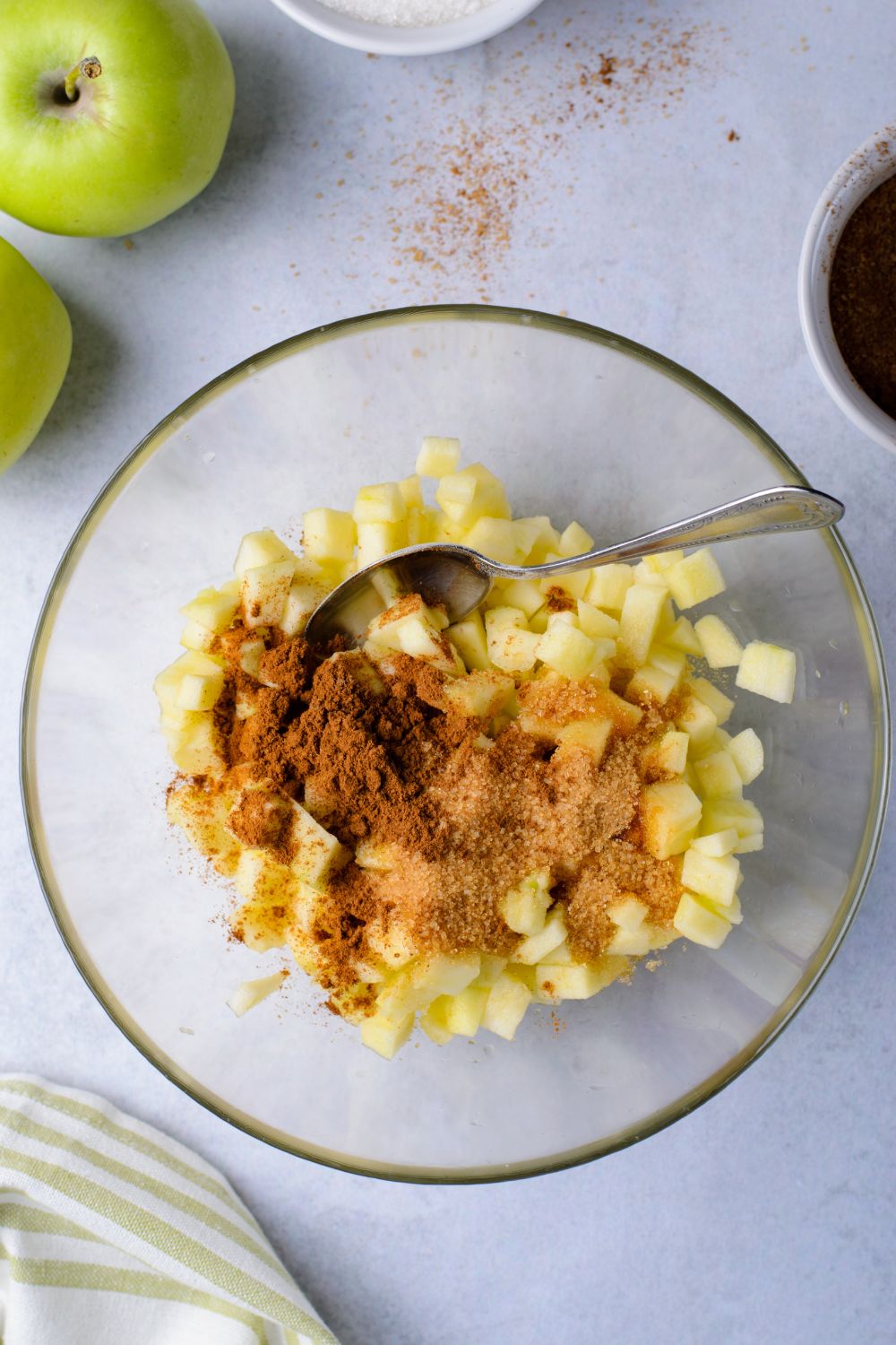 fresh diced apples in a bowl with some cinnamon on top and a spoon in bowl to mix 