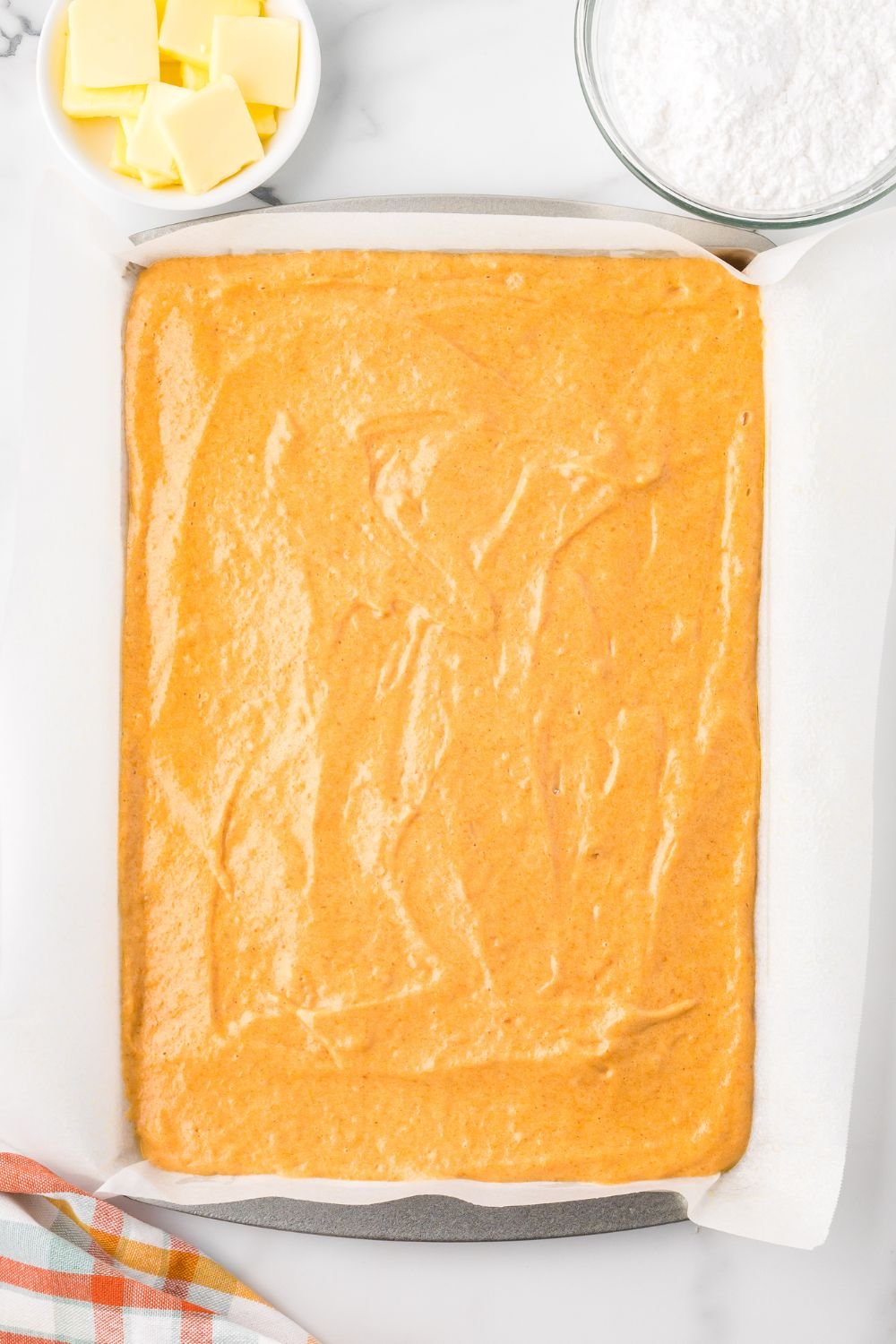 Pumpkin Cake Roll batter spread out in a baking pan sitting on table with parchment paper under it 