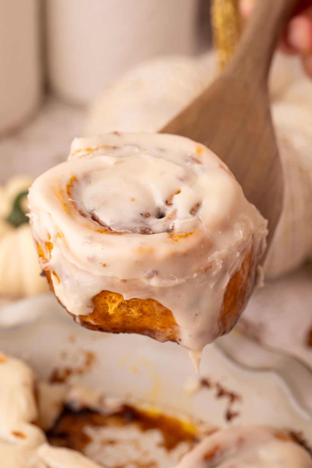 Pumpkin Cinnamon Rolls in a pie plate on table with a cinnamon roll scooping up out of pan, with a fall themed look on table 