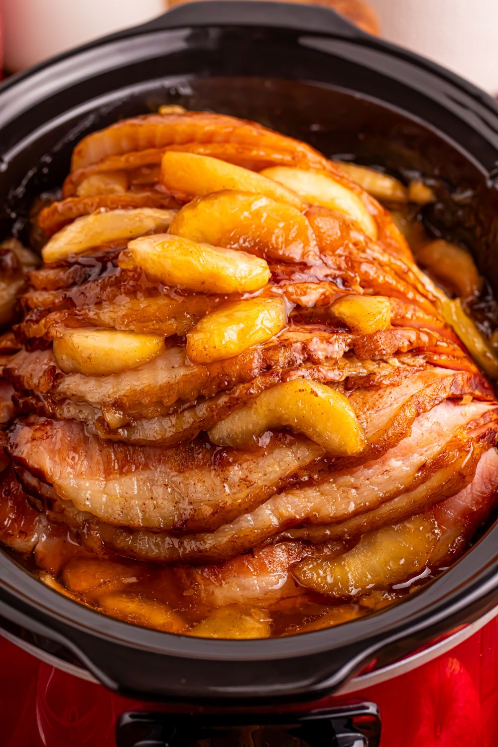 red slow cooker on table with a glazed apple spiral ham on table 